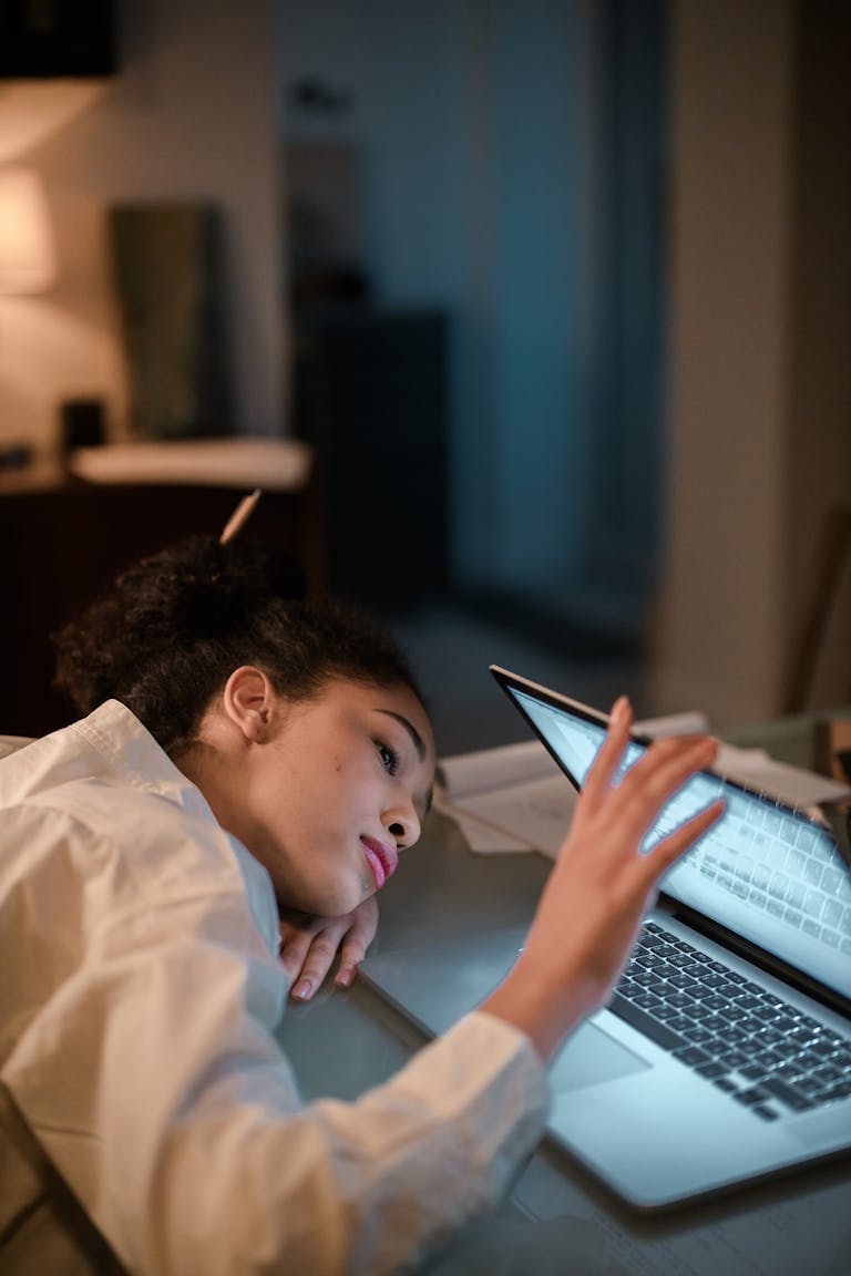 Exhausted woman lying on desk while using laptop late at night, depicting work from home fatigue.