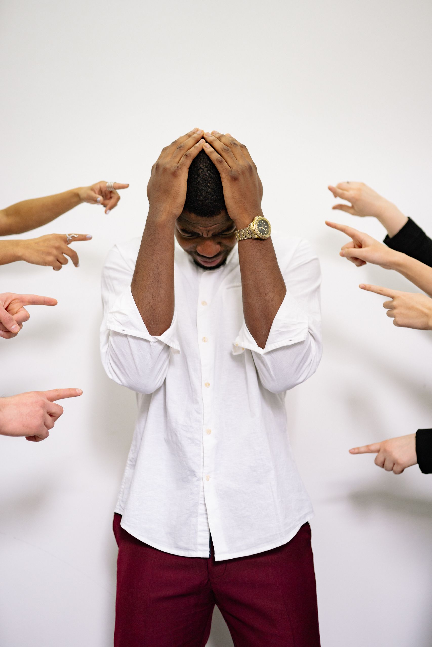 Frustrated man under stress as multiple hands point accusatory fingers at him.